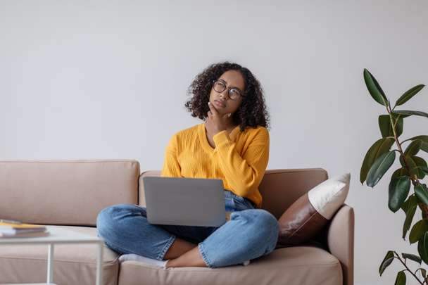 Átgondolt fiatal fekete nő laptoppal pc ül a kanapén, dolgozik online otthoni iroda, másolás hely - Fotó, kép