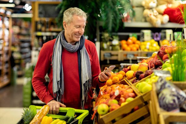 Cheerful senior customer purchasing at store, using phone - Photo, Image