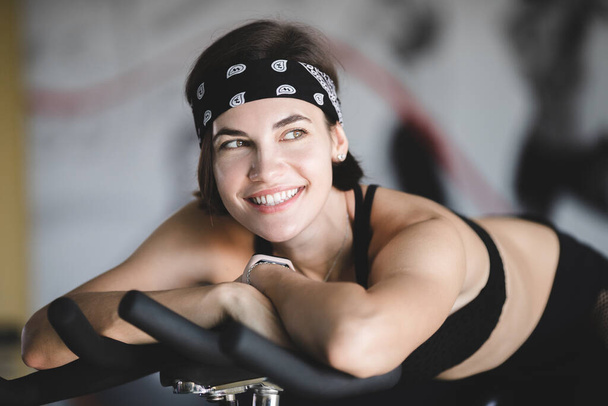 Portrait of an attractive white caucasian girl with a gorgeous smile. Girl on a stationary bike. Close-up portrait of a happy girl. - Φωτογραφία, εικόνα