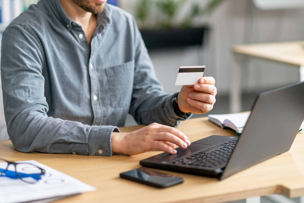 Online ödemeler için dizüstü bilgisayar ve kredi kartı kullanan, ofisinde oturan tanınmayan olgun bir adam. - Fotoğraf, Görsel