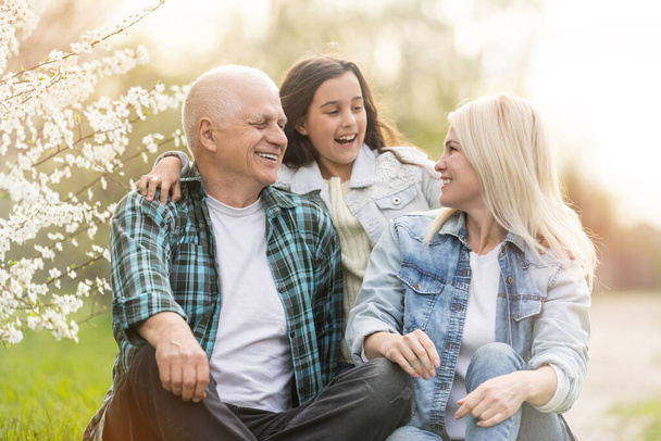 senior man grandfather sitting on outdoor in the park. Elderly retired male relax and enjoy outdoor activity together with daughter and granddaughter. Family relationship concept - Foto, imagen