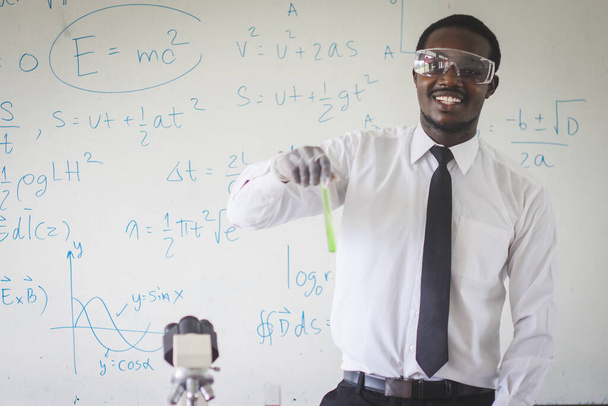 Αφρικανός καθηγητής φυσικής που διεξάγει πειράματα ανάμειξης υγρών σε φιάλη, βοηθός εργαστηρίου σε γυαλιά που παρουσιάζουν χημική αντίδραση στο μάθημα, έννοια χημείας - Φωτογραφία, εικόνα