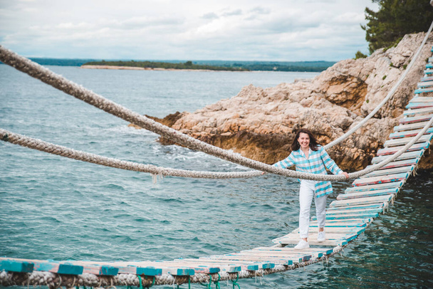 mulher cruzando suspensão ponte mar no fundo horário de verão - Foto, Imagem