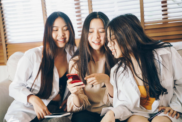 Beautiful asian women use smartphone social media together sitting on sofa in cozy room - Fotó, kép