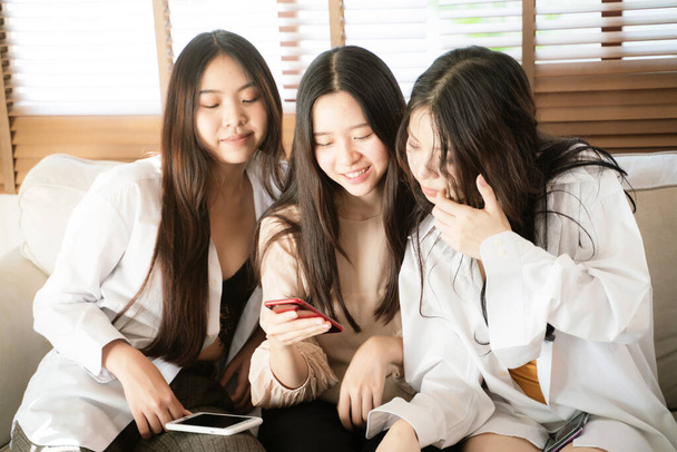 Belles femmes asiatiques utilisent les médias sociaux smartphone ensemble assis sur le canapé dans une chambre confortable - Photo, image