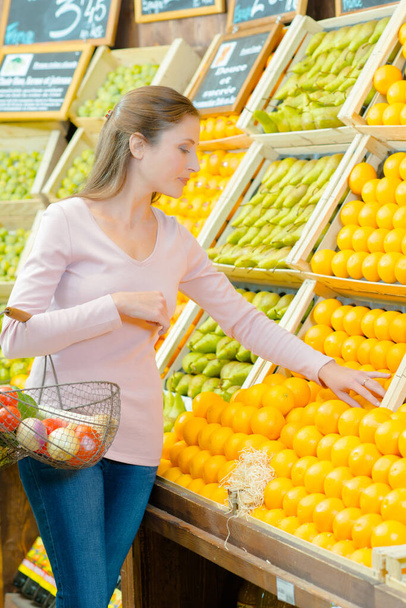 a lady is choosing oranges - Фото, изображение