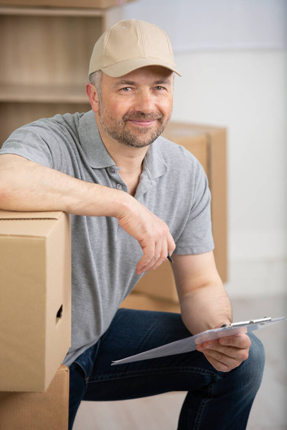 happy deliveryman with boxes and clipboard - Fotó, kép