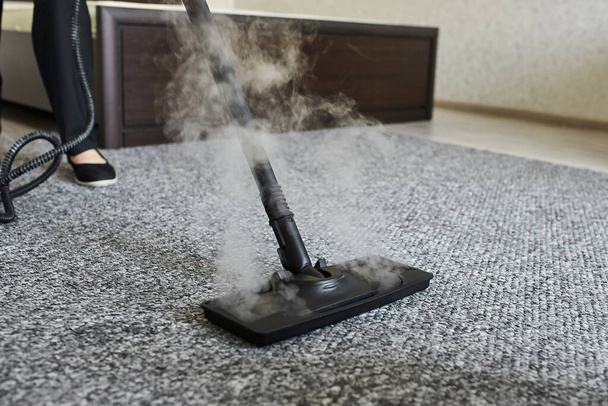 Takarító cég alkalmazottja eltávolítja a szennyeződést a szőnyegről lakásban professzionális gőztisztító berendezések közelről - Fotó, kép