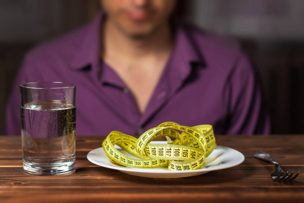 Diétás fogalom. Mérőszalag a tányéron. Ember eszik mérőszalag villával pohár vízzel, - Fotó, kép