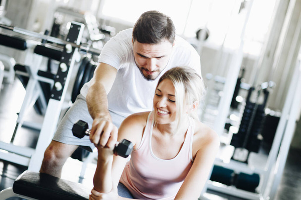 Oktató férfi tanítani a nők emelés súlyzó sport edzőteremben egészséges pár gyakorlat - Fotó, kép