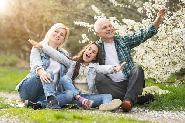 πρεσβύτερος παππούς κάθεται σε εξωτερικό χώρο στο πάρκο. Ηλικιωμένοι συνταξιούχοι άνδρες χαλαρώσετε και να απολαύσετε υπαίθρια δραστηριότητα μαζί με την κόρη και την εγγονή. Έννοια οικογενειακής σχέσης - Φωτογραφία, εικόνα
