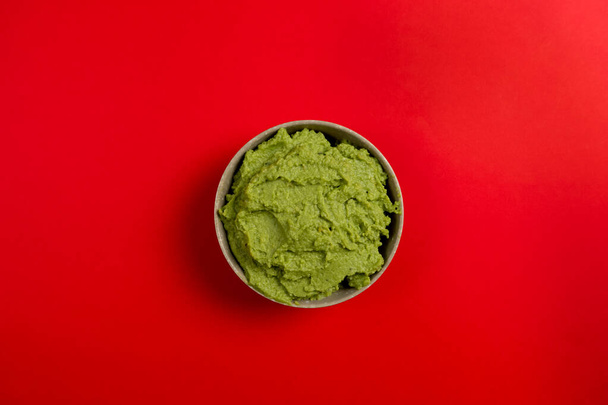 Top view of a ceramic bowl filled with the succulent guacamole sauce of Mexican origin on a red background. - Photo, Image