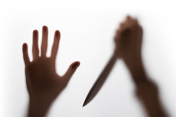Abstract blur hands silhouettes with knife behind glass foreground. - Фото, зображення
