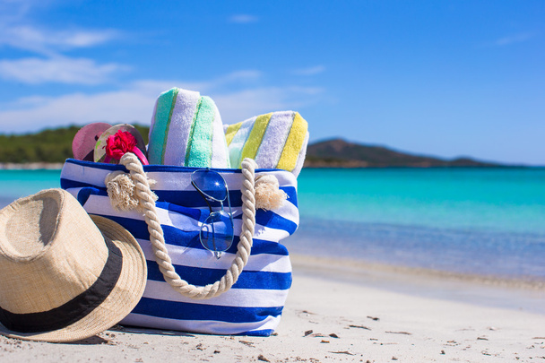 csíkos táska, szalmakalap, sunblock és a fehér homokos trópusi strand frizbi - Fotó, kép
