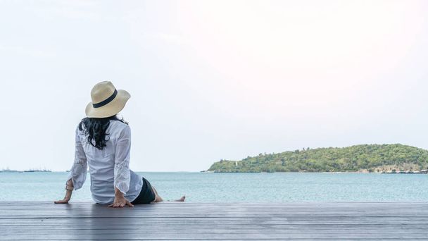Relajación de verano de la mujer asiática tómelo con calma felizmente sentado descansando en el muelle o la terraza del mar pacíficamente con el agua del océano y la isla tropical vista a la playa durante las vacaciones de viaje  - Foto, Imagen