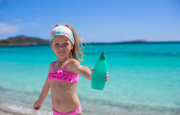 Little adorable girl in swimsuit with suntan lotion bottle - Photo, Image