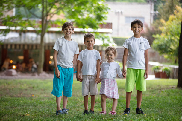 Three young boys and toddler girl in park. Friends or siblings playing outdoors. Summer vacations concept. - Foto, imagen