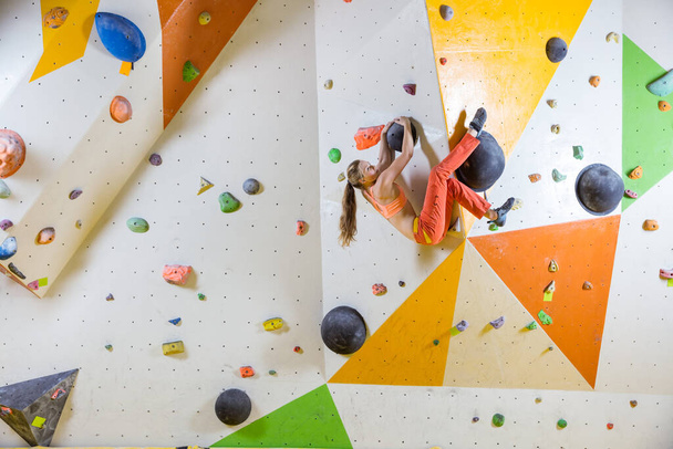 Mujer joven escaladora escalando una pared sobresaliente en un gimnasio de bouldering - Foto, imagen