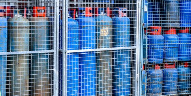 Gruppe blauer Propangasflaschen mit rotem Griff hinter Metallbolzen und -stange - Foto, Bild