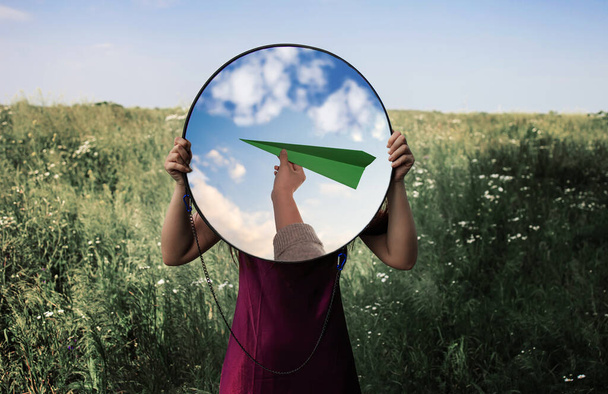 reflection in the mirror of hand holds a green paper plane in the sky. - Φωτογραφία, εικόνα