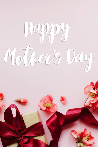 Χαρούμενη γιορτή της μητέρας. Ευτυχισμένες μητέρες ημέρα κείμενο και κουτί δώρου με κόκκινα λουλούδια σε ροζ φόντο επίπεδη θέσει. Κομψή ευχετήρια κάρτα λουλουδιών. Χειρόγραφα γράμματα. Ημέρα μητέρων - Φωτογραφία, εικόνα