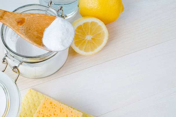 Open jar of baking soda with a wooden spoon on top, vinegar, cut lemon. top view, space for text. The concept of organic removing stains on kitchen . High quality photo - Foto, imagen