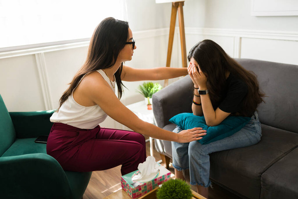 Depressed girl covering her face and crying during a therapy session. Professional psychologist comforting a teen patient - Foto, Imagem