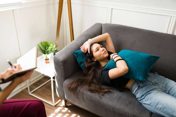 Fatiguée jeune fille triste reposant sur le canapé pendant une séance de thérapie pour obtenir de l'aide et des conseils pour sa santé mentale - Photo, image