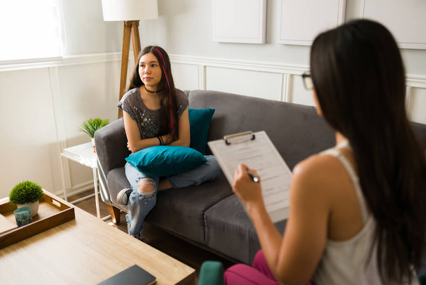 Angry teen girl having a negative attitude during a therapy session with a psychologist - Photo, Image
