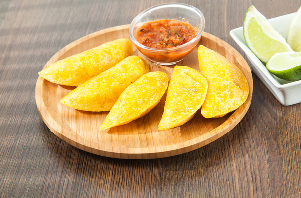 Colombian empanada with spicy sauce on wooden background. typical dish, to enjoy in special moments - Photo, image