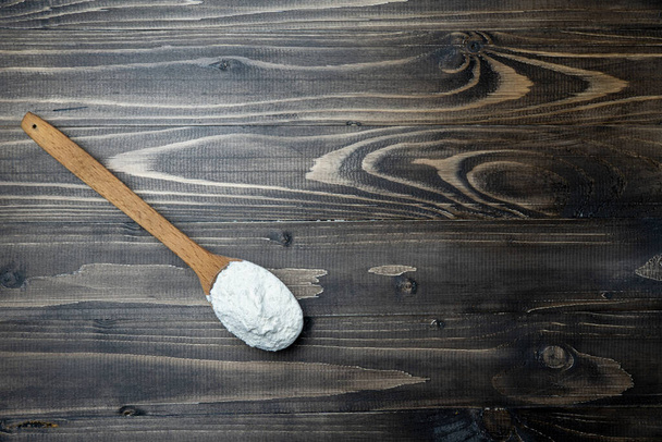Whole flour in spoon on dark vintage wooden background. Close up view. Preparations for homemade baking. Basic ingredients for baking. Wheat flour on wooden spoon.  - Valokuva, kuva