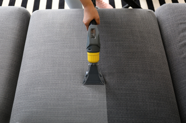 Woman removing dirt from sofa with vacuum cleaner at home, top view - 写真・画像