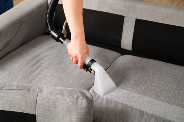 Man removing dirt from grey sofa with vacuum cleaner in room, closeup - 写真・画像