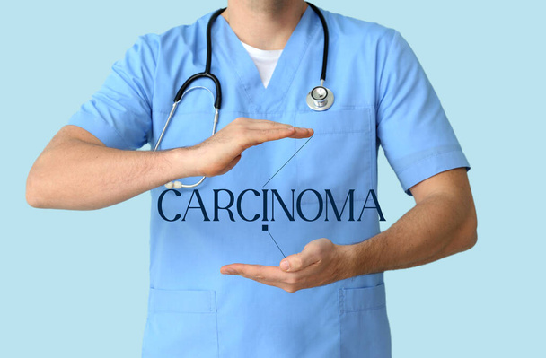 Man arts met woord CARCINOMA op virtueel scherm tegen blauwe achtergrond - Foto, afbeelding