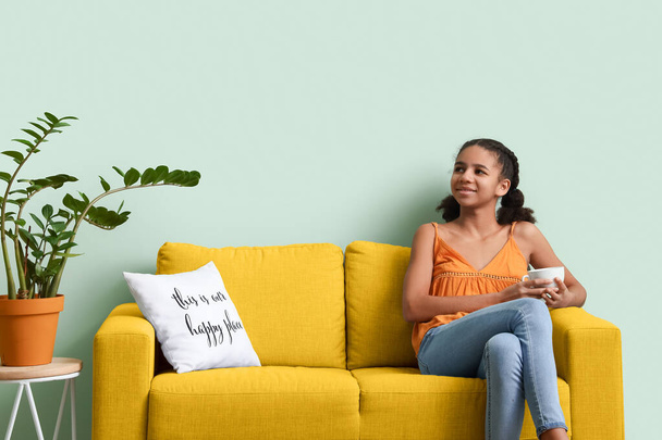 Афроамериканська дівчина-підліток п'є чай, сидячи на дивані.   - Фото, зображення