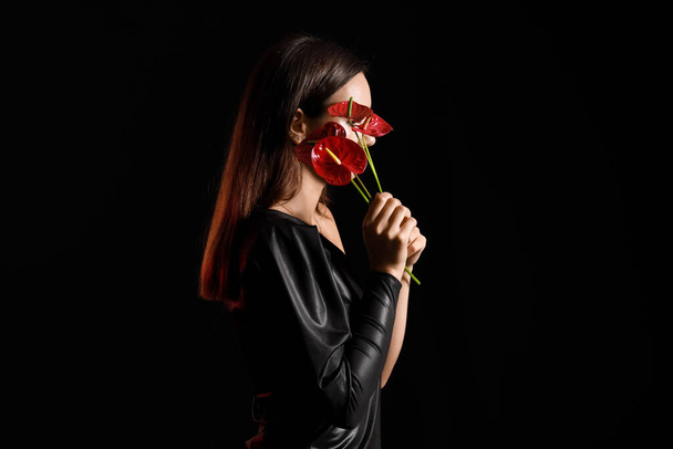 Young woman closing face with bouquet of anthurium flowers on black background - Fotó, kép