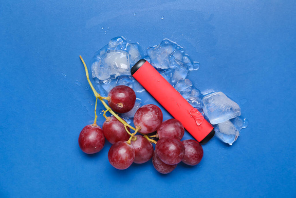 Cigarrillo electrónico desechable, uvas y cubitos de hielo sobre fondo azul - Foto, imagen