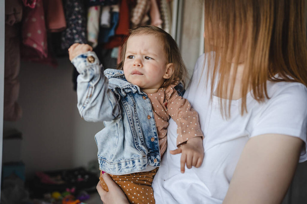 Small caucasian baby girl infant child with her mother dressing or undressing small daughter at home childhood parenthood and growing up family concept real people copy space - Fotografie, Obrázek