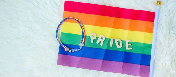 LGBTQ, Duhová vlajka a náramek na bílém pozadí. Podpora lesbických, gayů, bisexuálů, transsexuálů a homosexuálů komunita a hrdost měsíční koncept - Fotografie, Obrázek