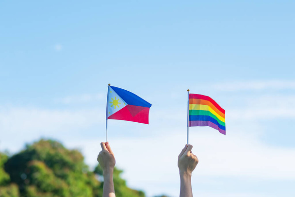 χέρια που δείχνουν ΛΟΑΤΚΙ Rainbow και Φιλιππίνες σημαία στο φόντο της φύσης. Υποστήριξη Lesbian, Gay, Bisexual, Transgender και Queer κοινότητα και Pride μήνα έννοια - Φωτογραφία, εικόνα