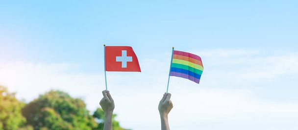hands showing LGBTQ Rainbow and Switzerland flag on nature background. Support Lesbian, Gay, Bisexual, Transgender and Queer community and Pride month concept - Fotografie, Obrázek
