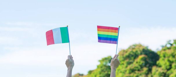 hands showing LGBTQ Rainbow and Italy flag on nature background. Support Lesbian, Gay, Bisexual, Transgender and Queer community and Pride month concept - 写真・画像