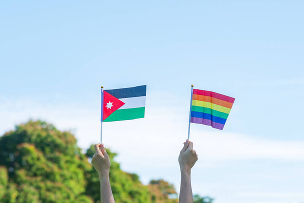 hands showing LGBTQ Rainbow and Jordan flag on nature background. Support Lesbian, Gay, Bisexual, Transgender and Queer community and Pride month concept - Fotografie, Obrázek