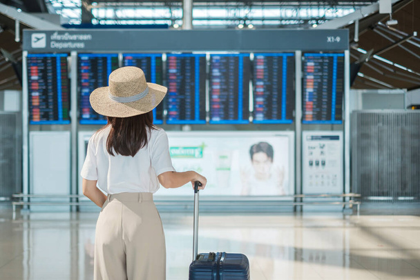 Young woman hand holding luggage handle before checking flight time in airport, Transport, insurance, travel and vacation concepts - Photo, Image
