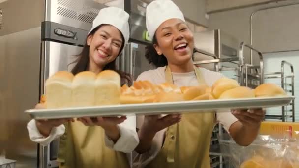 Portrét profesionálních kuchařek v uniformě, dívajících se na kameru s veselým úsměvem a pyšných s tácem chleba v kuchyni. Přítel a partner pekařských jídel a čerstvé denní pekařství zaměstnání. - Záběry, video