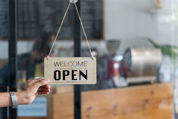 Kaukasier wechselt das Schild am Eingang seines kleinen Cafés von geschlossen in geöffnet. Konzept für Essen und Trinken für Kleinunternehmen. - Foto, Bild