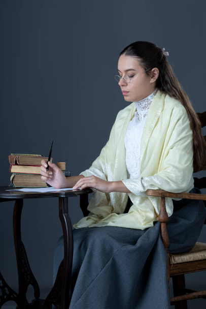 Βικτωριανή ή Εντουαρντιανή γυναίκα κάθεται σε μια καρέκλα και διαβάζει ένα βιβλίο. - Φωτογραφία, εικόνα