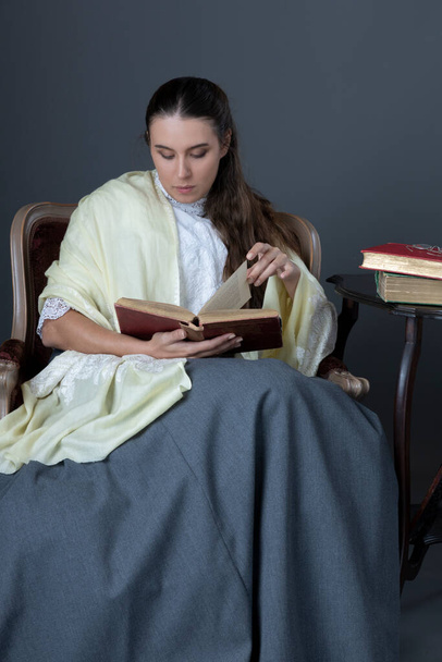 Eine viktorianische oder edwardische Frau sitzt auf einem Stuhl und liest ein Buch - Foto, Bild