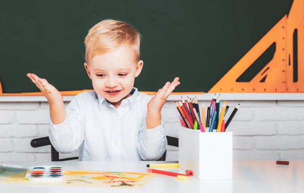 Little student boy happy with an excellent mark. Kid is learning in class on background of blackboard. Little children at school lesson. - 写真・画像