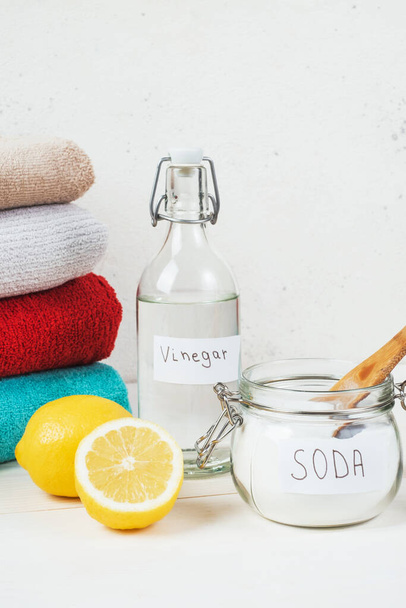 Baking soda in jar with a wooden spoon on top, vinegar, cut lemon, folded towel on a white background. The concept of organic removing stains on clothes. High quality photo - Photo, image